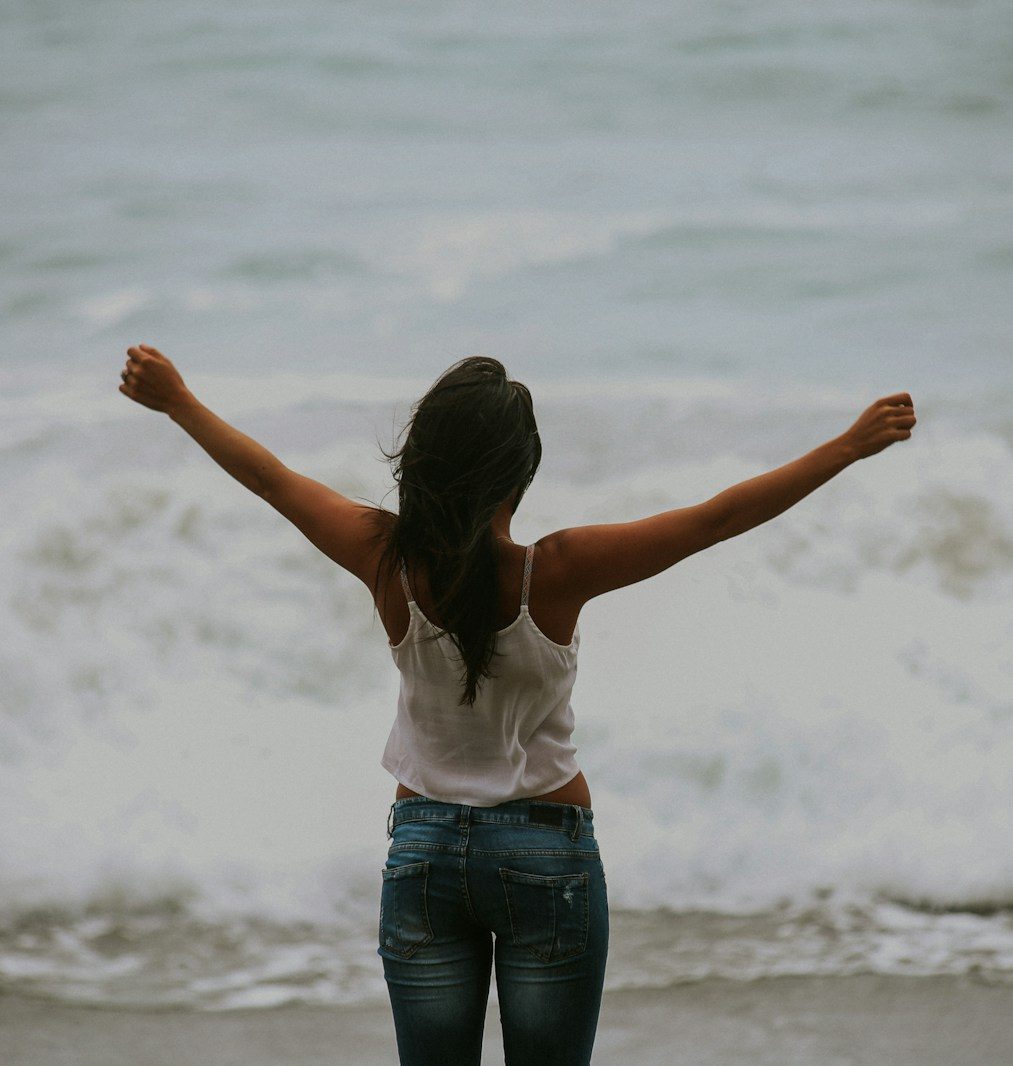woman in white spaghetti strap top standing on the seashore