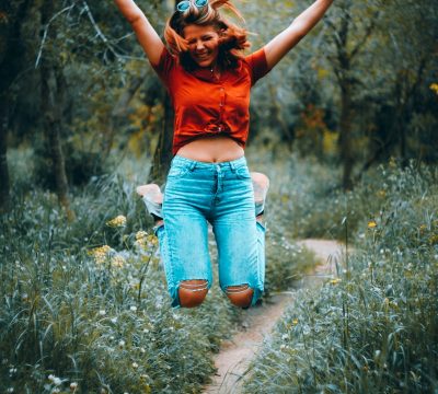 woman in orange t-shirt and blue denim jeans standing on green grass field during daytime